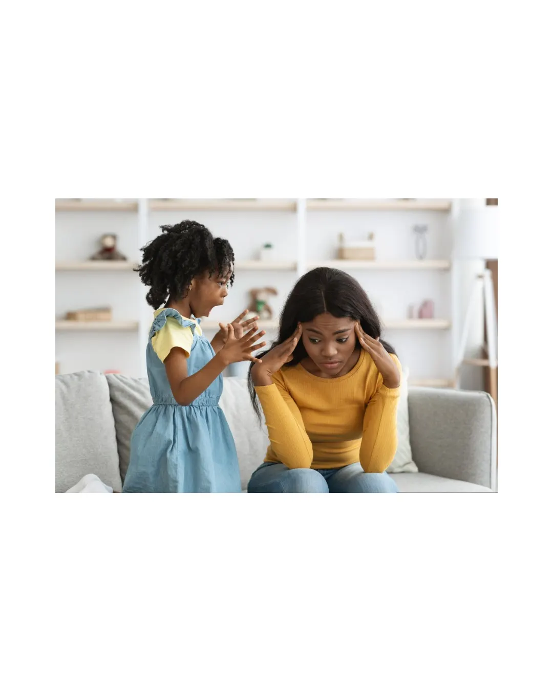 A woman sitting on a couch looking overwhelmed, with a child standing behind her