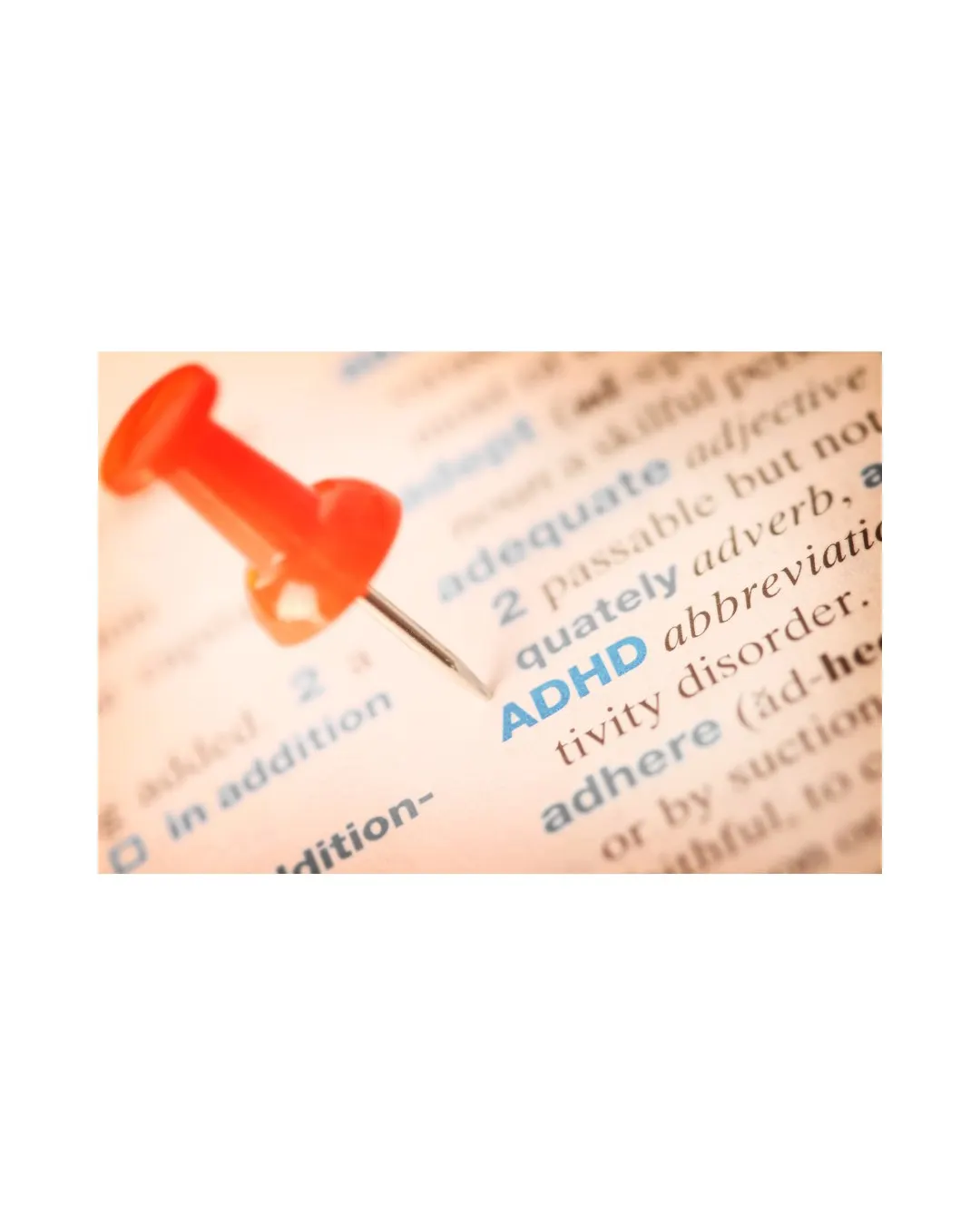A red pushpin on a dictionary page highlighting the word ADHD